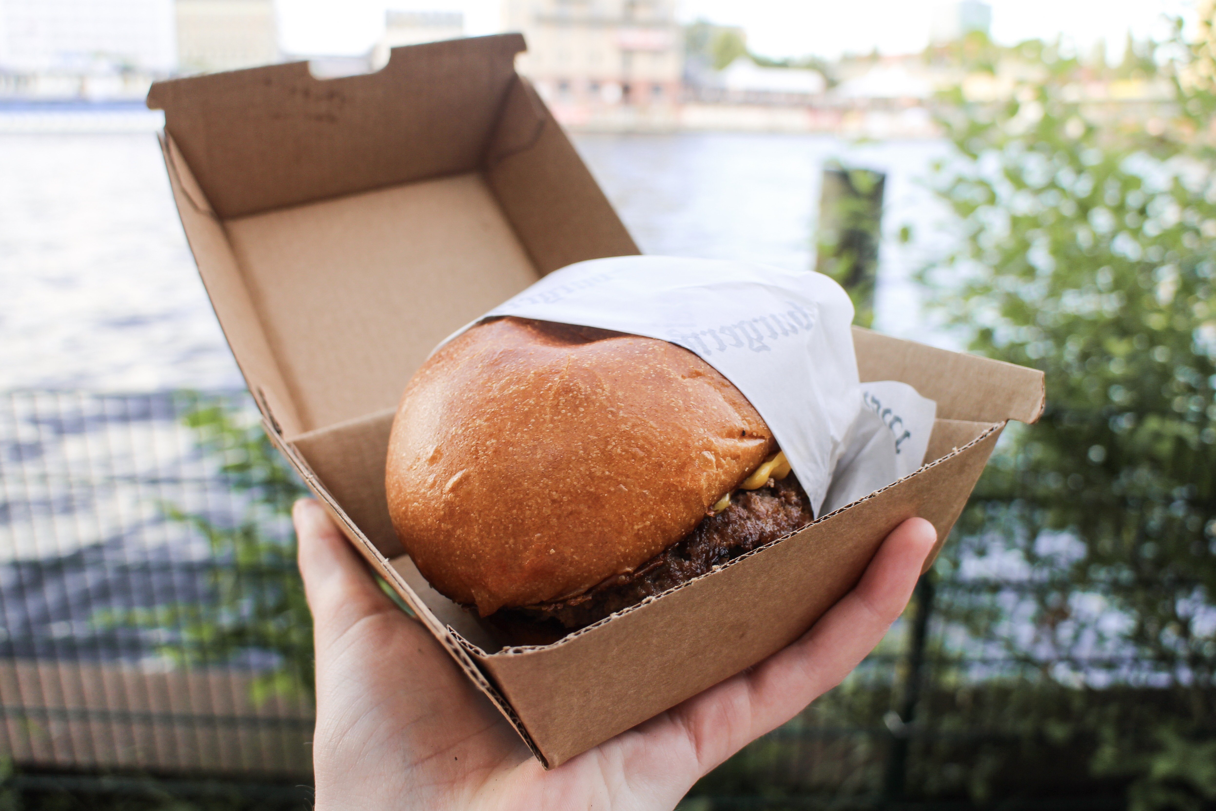 A burger in being held against the backdrop of the River Spree in Berlin