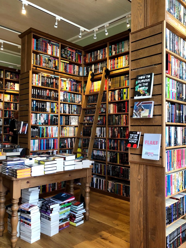 Topping & Company, Booksellers of Edinburgh. The interior is a maze of tall bookcases, completely filled with different fiction titles. a rolling ladder is in front of the display.