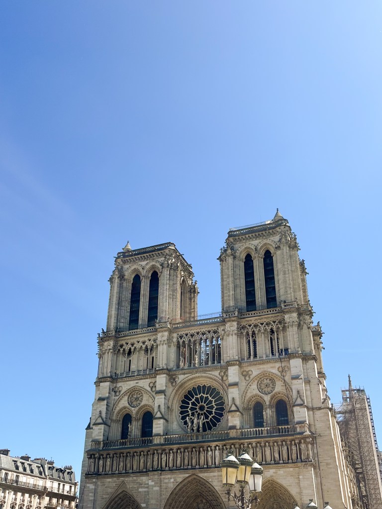 the still intact front of notre dame against a blue sky with immense scaffolding seen in the background as part of the restoration