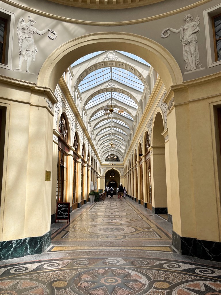 a covered passage. the ceiling is made mainly of glass windows and store fronts are shaped arches
