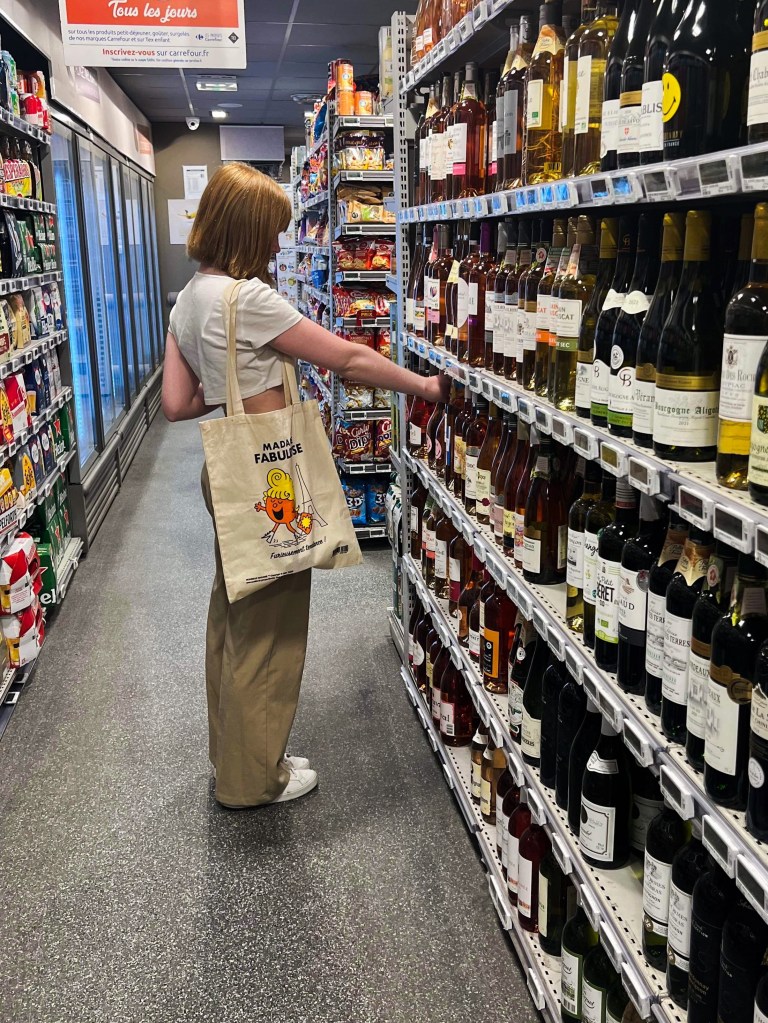 redheaded gal with a tote bag shopping for wine at the supermarket