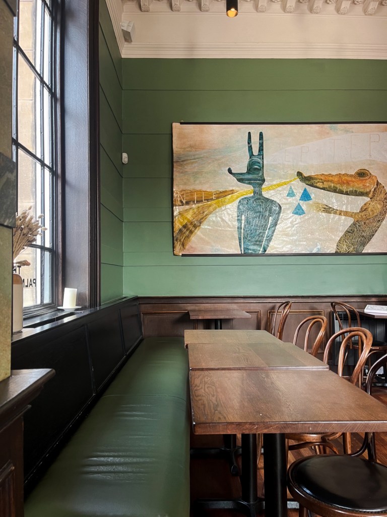 a restaurant interior. wooden tables and chairs with green walls as the table are up against a wall with large windows.