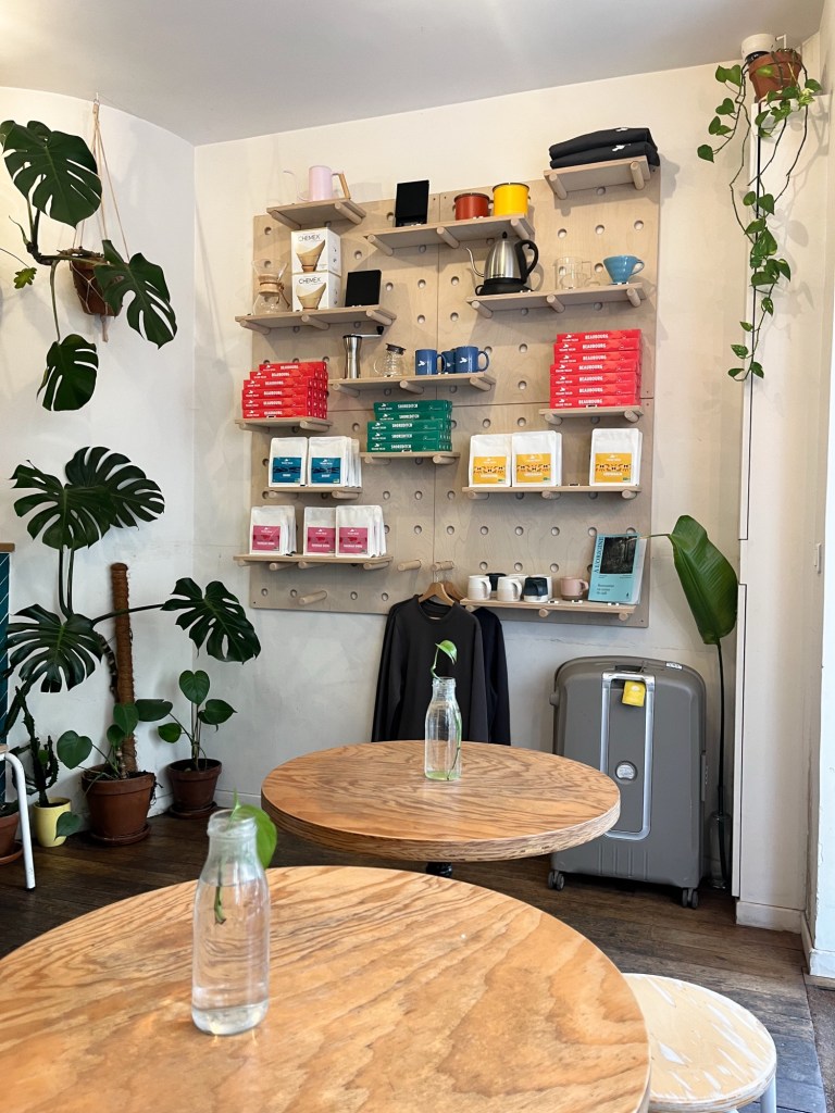the merchandise shelf of a coffee shop. on it are bags of coffee beans and pods amongst branded t-shirts