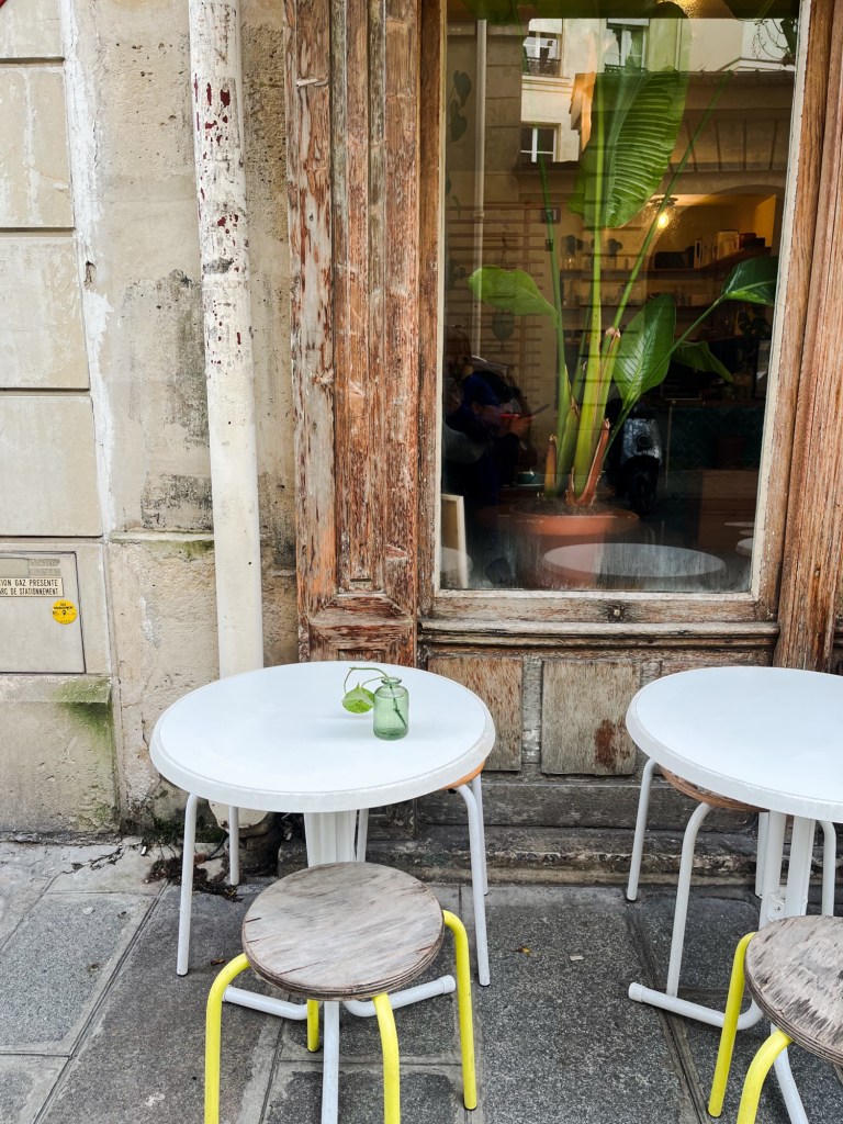 the exterior of a coffee shop. there is some distressed wood around the window frames and some tables on the pavement