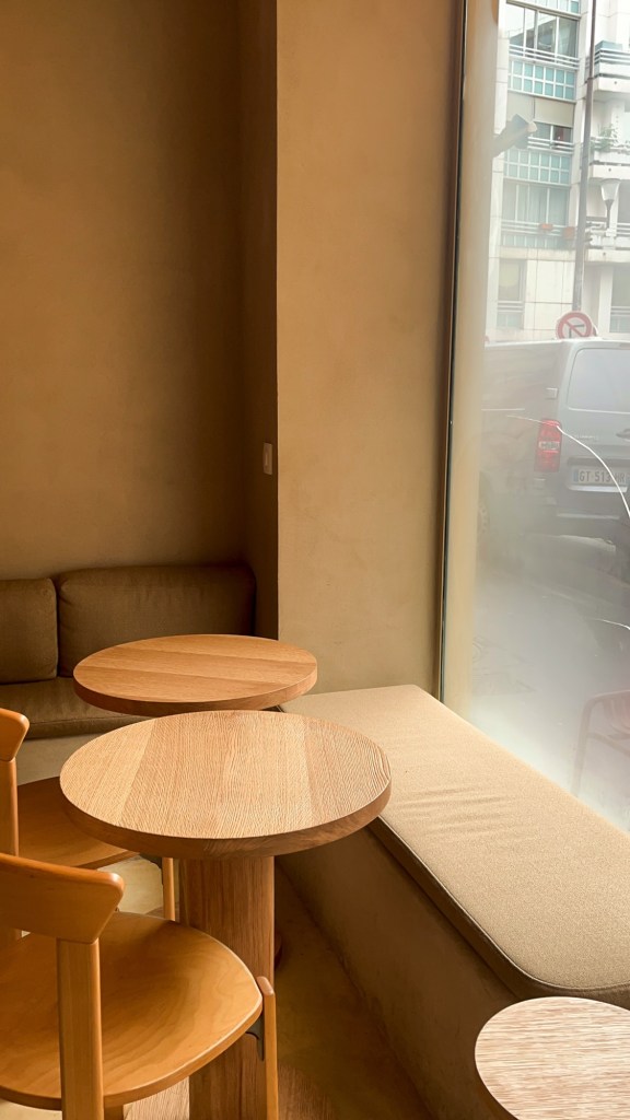 the interior of a coffee shop. There is a minimal colour palette brightened by a large window