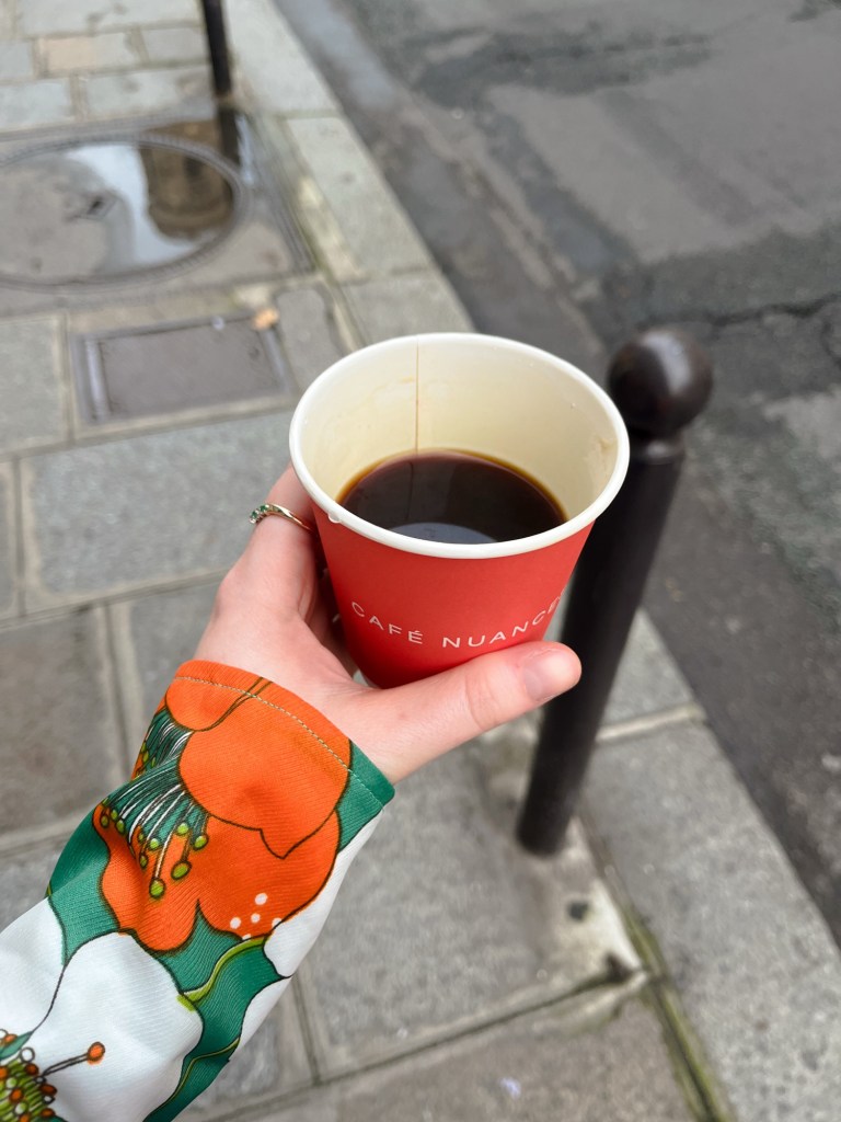 an orange paper cup filled with black coffee held by somebody wearing a shirt of similar colour