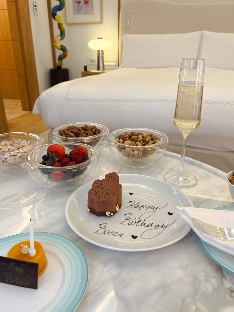 an extravagant spread of nibbles on a marble coffee table. There are lots of bowls of nuts, a chocolate birthday cake and champagne flutes