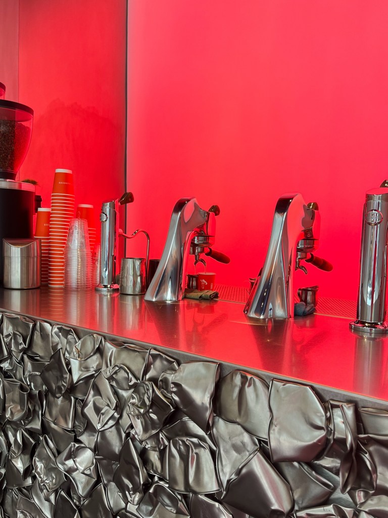 a modbar coffee machine sits on top of a stainless steel coffee bar. The walls of the coffee shop are luminous red