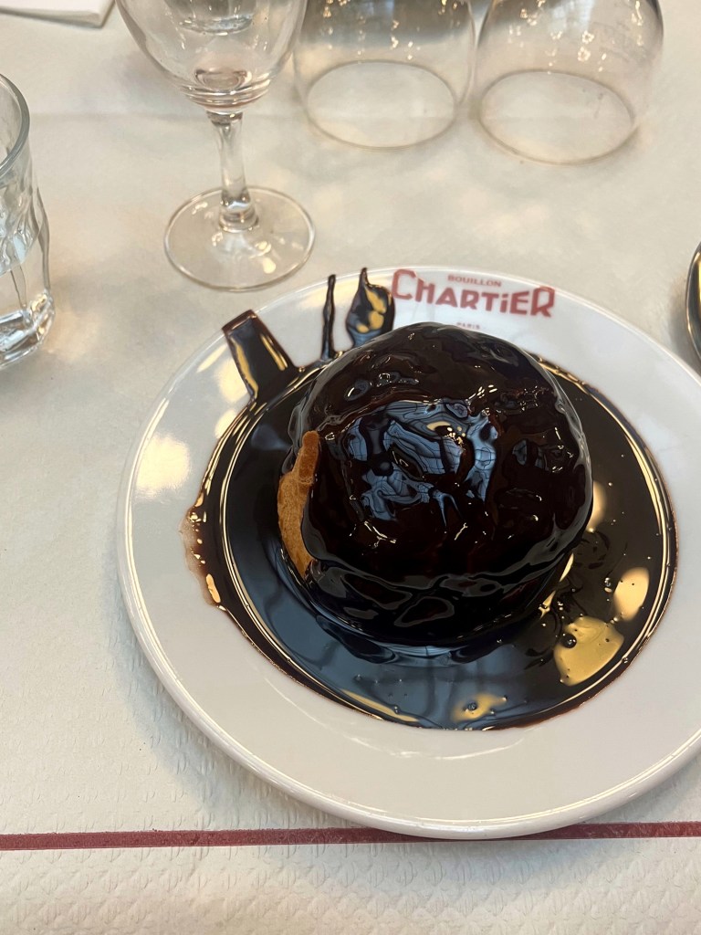 A large profiterole takes up a whole plate, drowing in chocolate sauce