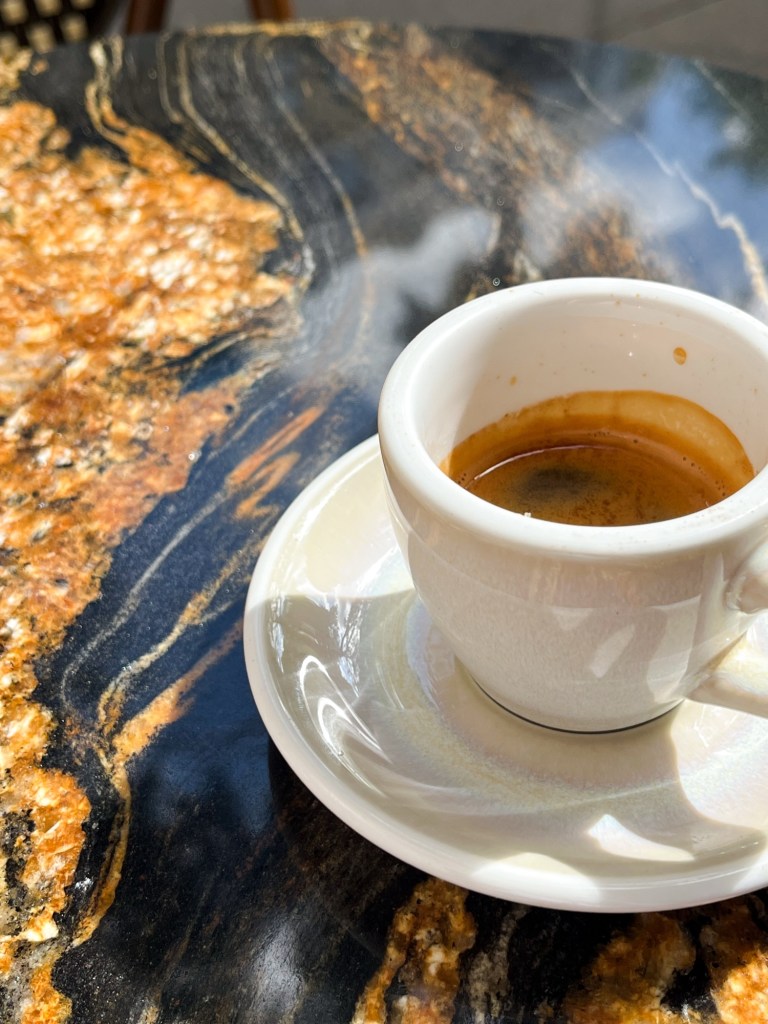 a single espresso in a small white cup sits on a marble table