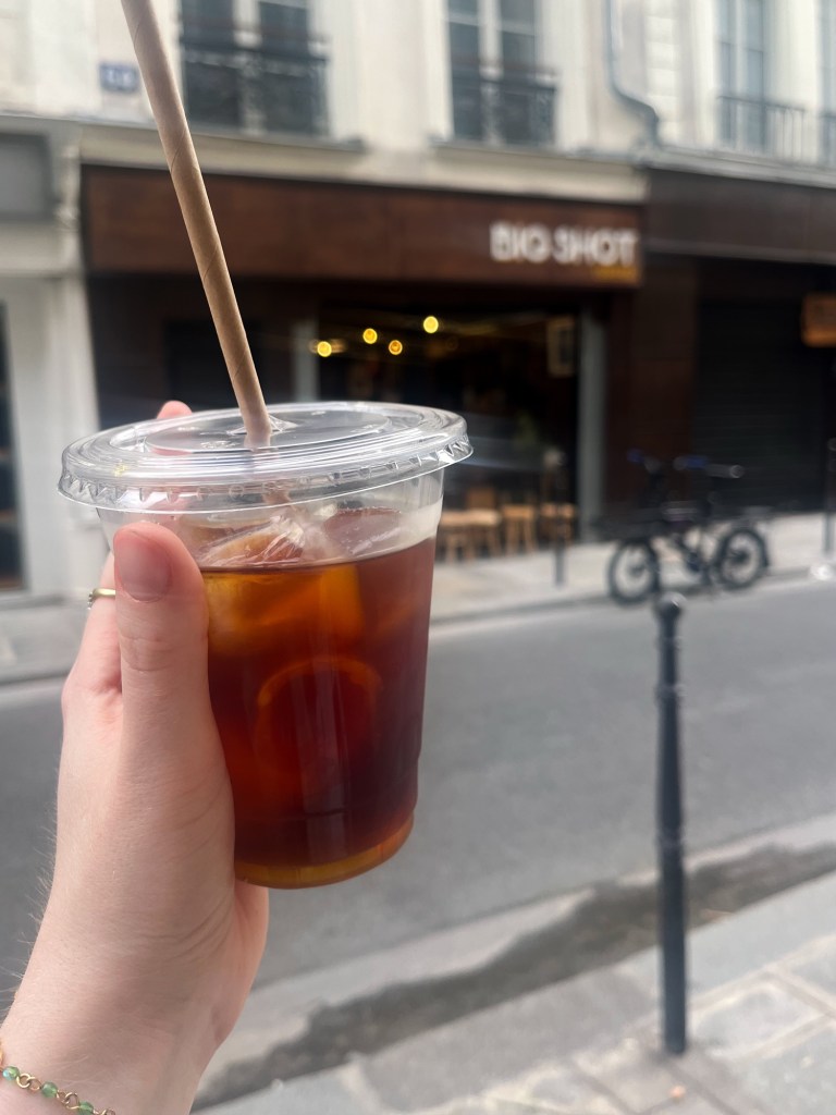 a takeaway iced coffee in front of a coffee shop facade