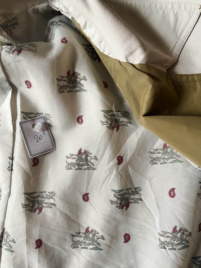 it showcases the lining of a trench coat. There is a repeated pattern of an illustration featuring horse riders going to hunt