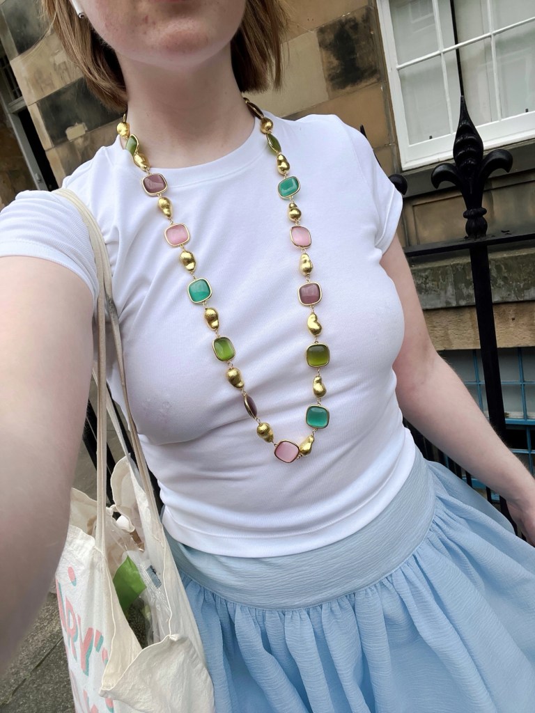 A selfie highlighting the photographer's outfit. She is wearing a white t-shirt and light blue bubble skirt. As well as a long necklace with chunky gold beads and colourful stones