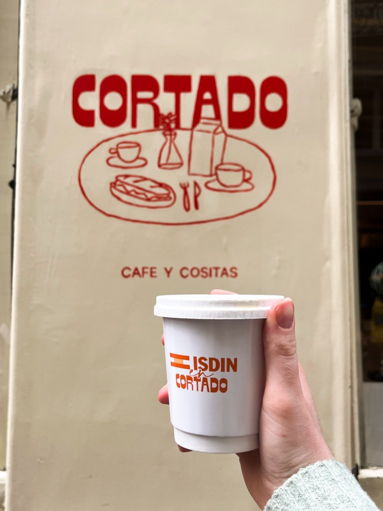 a coffee cup with a spanish flag  is held up in front of a coffee shop sign