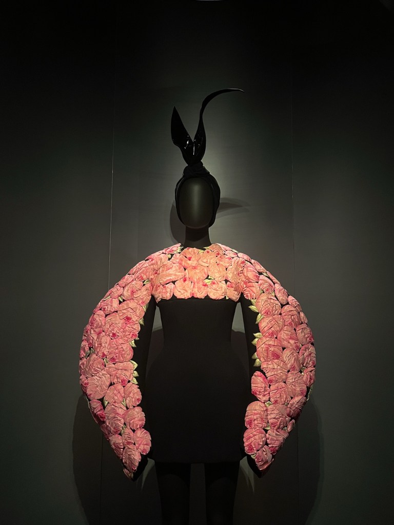 a sculptural black dress with pink roses adorning the chest, shoulders and arms