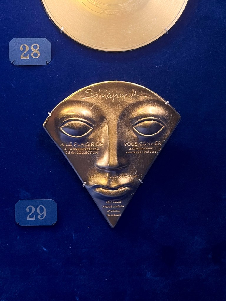 a golden plate shaped as a face engraved with invitation details