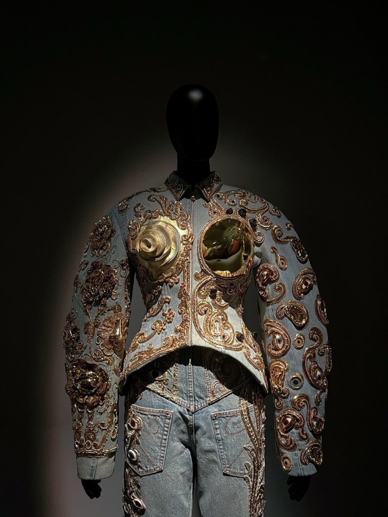 A structure denim jacket with exaggerated shoulders, cones on the chest and excessive gold embellishment. 